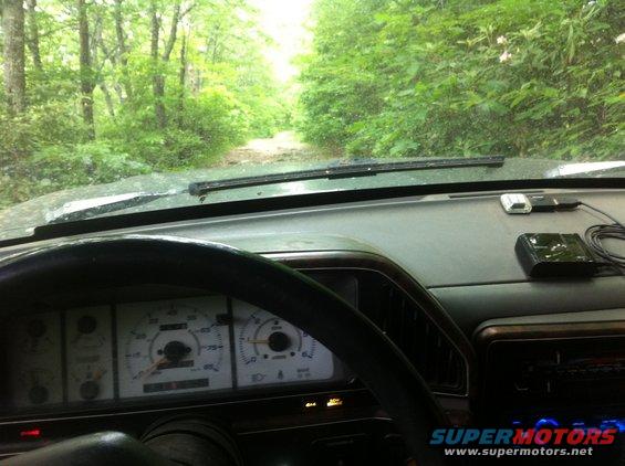 1988 Ford Bronco interior with dashboard and gauges visible, driving on a dirt road