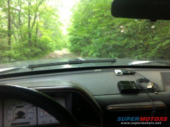 1988 Ford Bronco interior view, driving on dirt road in forest. Dashboard, steering wheel, and gauges visible