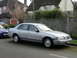 1999 Ford Fairlane - A silver sedan is parked on a residential street next to a blue car.