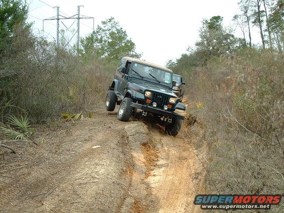 Black Jeep Wrangler driving off-road on a dirt trail with another vehicle behind it