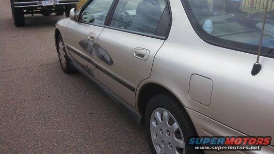 Silver sedan with a large black decal on the driver's side door, parked next to a black pickup truck