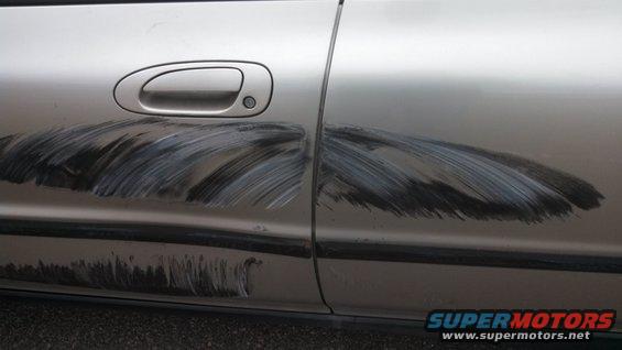 Silver car door with extensive scratch marks across the front and rear sections, obscuring the original paint