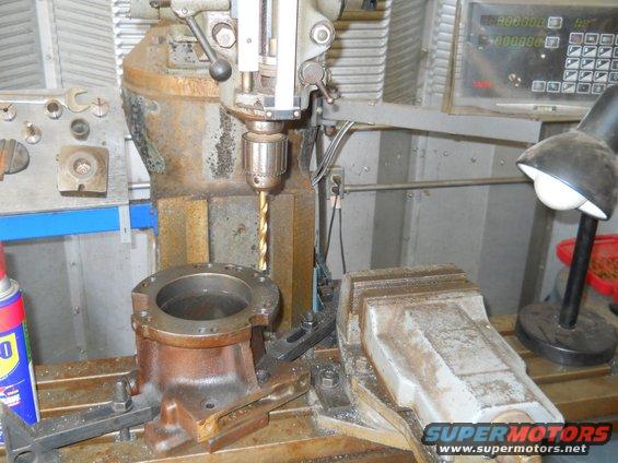 Drill press machining a metal part held in a vise