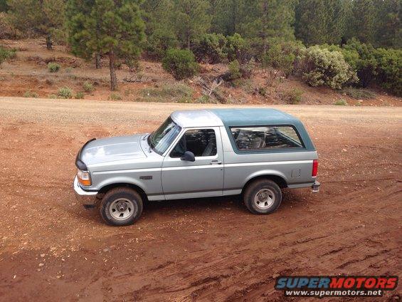 Silver Ford Bronco with a green top parked on a dirt road