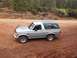 1996 Ford Bronco - This silver Ford Bronco with a green top is parked on a dirt road with trees in the background.