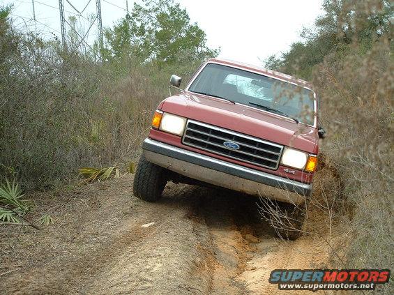 Red 1995 Ford Bronco 4x4 driving off-road on a dirt path