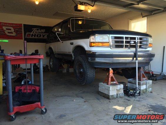 Ford Bronco on jack stands in a garage. It has a two-tone paint job and a chrome grille