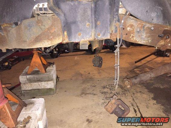 Rusted vehicle frame and suspension components supported by jack stands in a garage