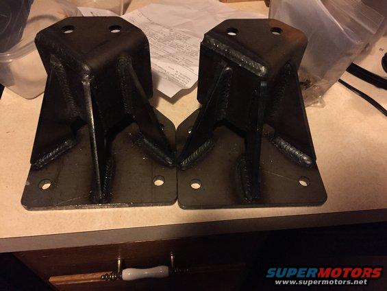 Two welded steel brackets with four bolt holes each, sitting on a counter