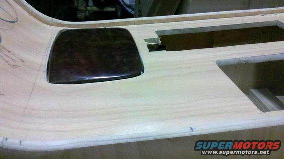 Unfinished wooden dashboard panel with a dark rectangular insert and cutouts for components