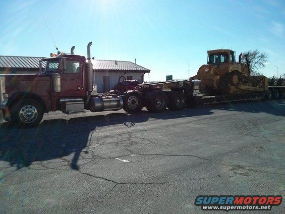 Maroon semi-truck towing a yellow bulldozer on a flatbed trailer