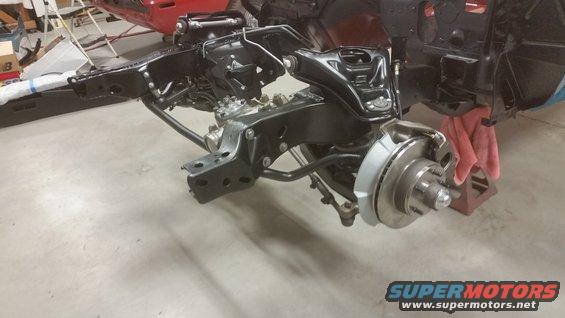 Front suspension and chassis components of a car, possibly undergoing restoration. Disc brake assembly visible