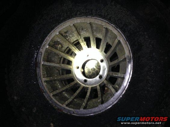 Close-up of a dirty, silver alloy wheel with a multi-spoke design, mounted on a tire