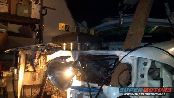 Engine bay with work light, wooden beam, and level. White vehicle