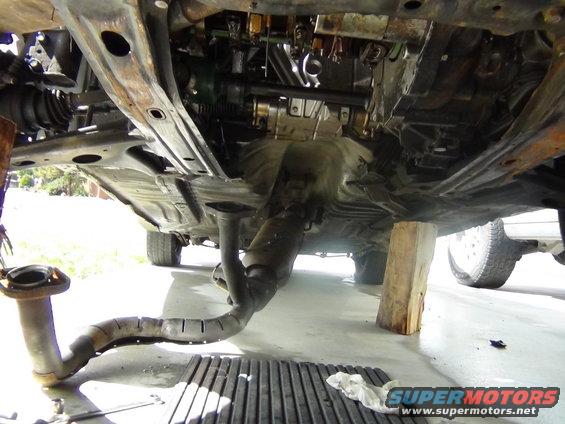 Underside of a car with exhaust system removed, engine components visible, and car supported by wooden blocks
