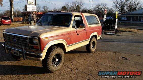 1986 Ford Bronco with red and tan two-tone paint, parked on cracked asphalt