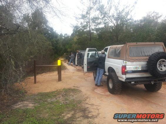 White Ford Bronco with a tan soft top and spare tire on the back, parked on a dirt road