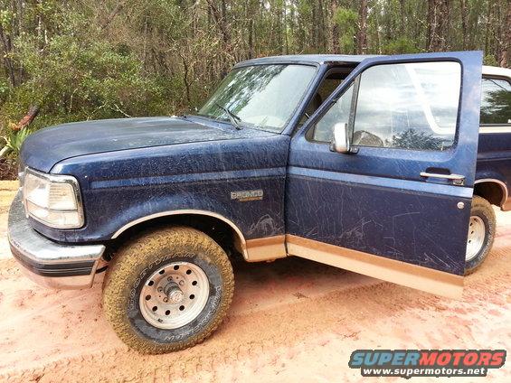 Blue 1994 Ford Bronco with driver's door open, parked on a dirt road