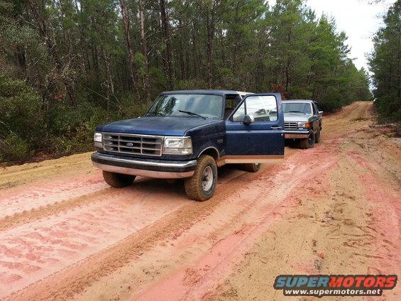 Blue Ford F-Series truck with driver's door open, parked on a dirt road