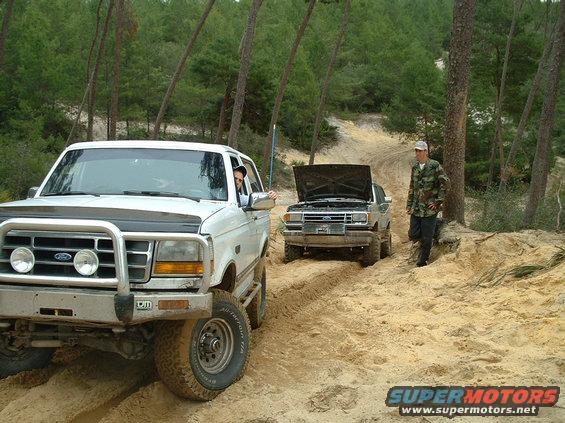 White Ford Bronco with a brush guard and off-road tires, parked on a sandy track
