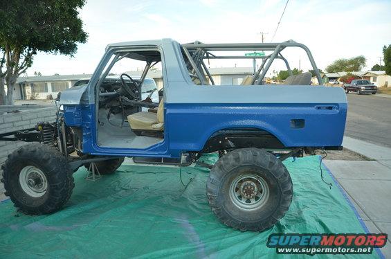 Off-road vehicle body, blue and gray, with roll cage, on green tarp. Front end is disassembled
