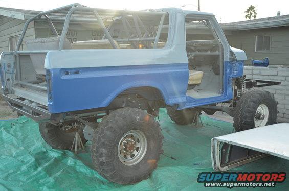 Modified Ford Bronco with roll cage, lifted suspension, and large tires, sitting on jack stands