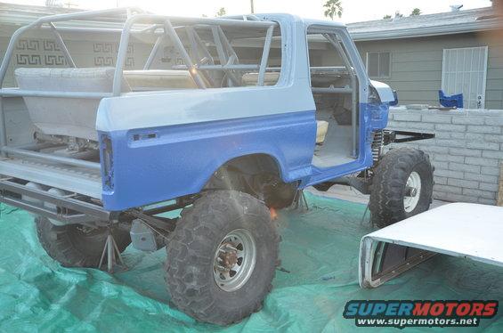 SUV body with roll cage, lifted suspension, and large tires, partially disassembled. A separate roof section is nearby