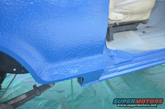 Blue textured vehicle door sill and interior with beige seat. Leaf spring visible underneath