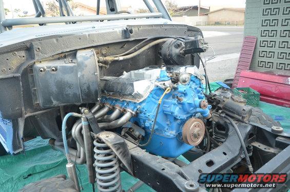 Engine bay with a blue engine, headers, and suspension components. The vehicle appears to be under construction