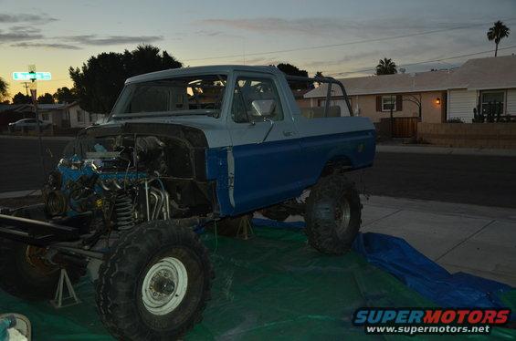 Ford Bronco with engine exposed, raised on jacks, with blue and gray paint. Dusk sky