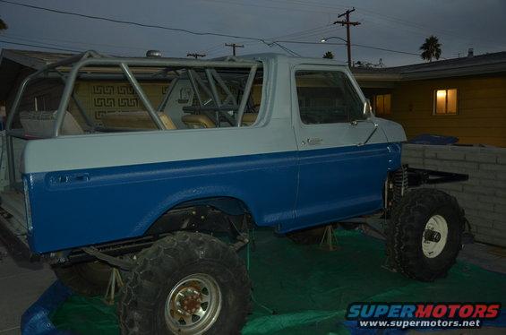 Blue and white 1979 Ford Bronco with roll cage, lifted on jacks