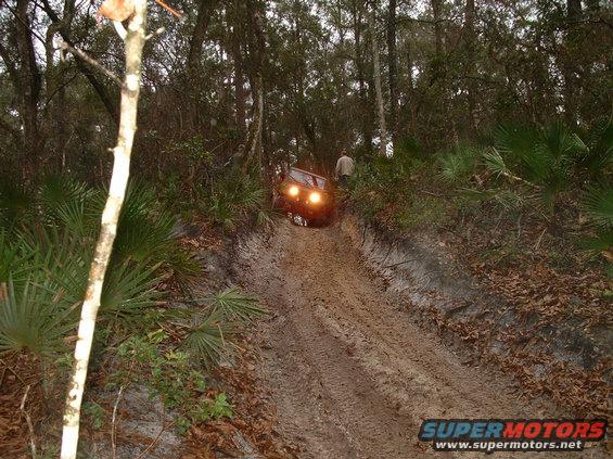 Red SUV climbing a steep, muddy trail through a forest