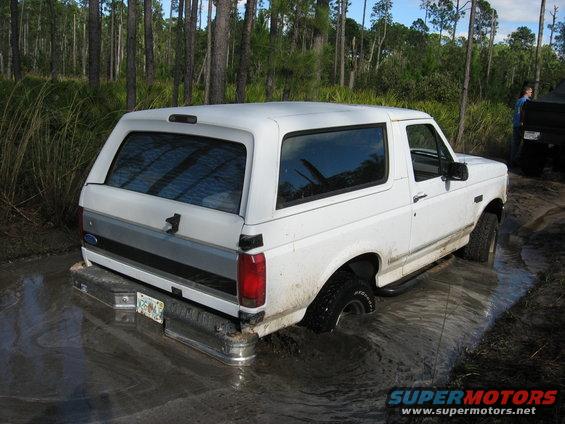 White 1994 Ford Bronco stuck in mud, rear 3/4 view