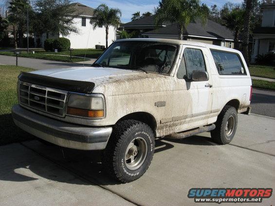 White 1994 Ford Bronco covered in mud, parked in a driveway