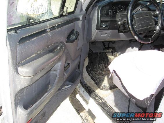 Interior of a dirty white Ford truck, driver's side door open, showing worn gray upholstery and dashboard