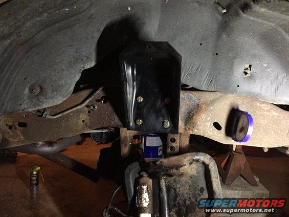 Vehicle frame with new black bracket bolted to rusty crossmember, blue bushing on jack stand