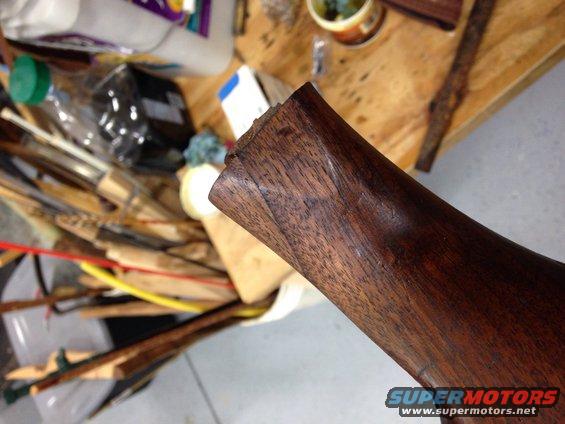 Wooden trim piece with visible grain and damage at the end, on a workbench with tools and supplies