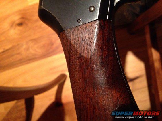 Close-up of a wooden grip and metal receiver of a firearm, with a Supermotors.net watermark