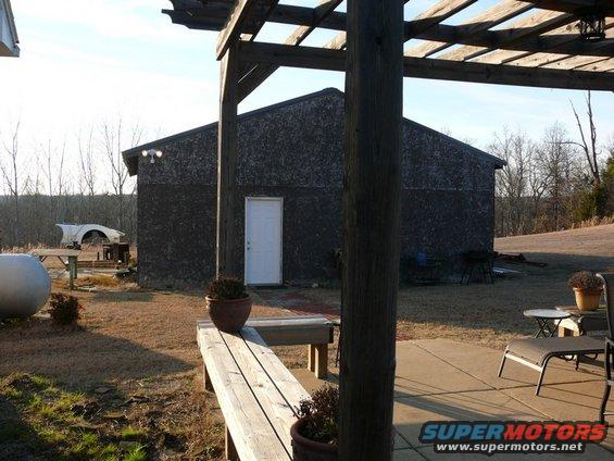 White car fender and wheel arch on a table outdoors, with a dark building and trees in the background