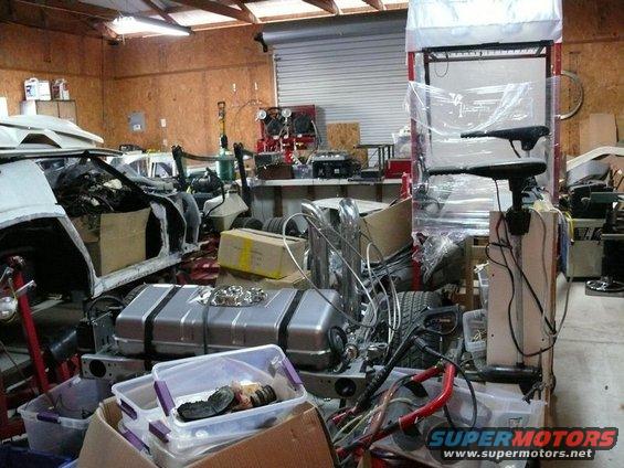 Disassembled vehicle body and parts in a cluttered garage, including a fuel tank and engine components