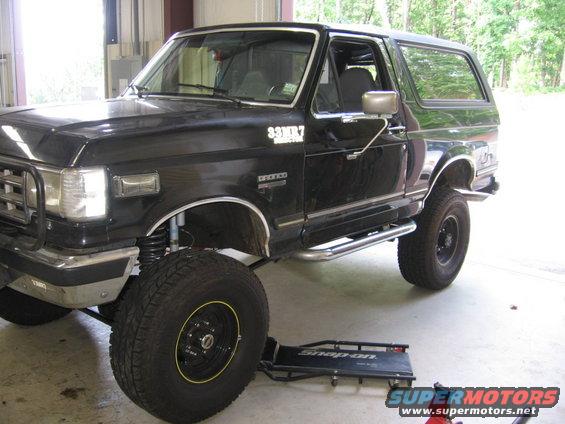 Black Ford Bronco with custom wheels and side steps, front wheel elevated on a creeper