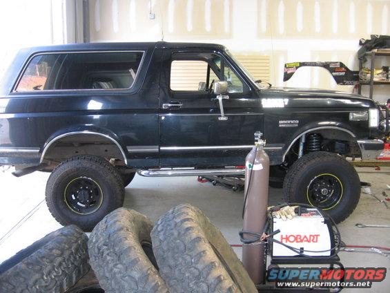 Black Ford Bronco parked in a garage with spare tires and welding equipment nearby