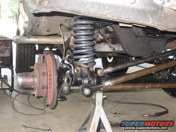 Close-up of a truck's front suspension and brake assembly, with a welding machine in the background