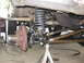1988 Ford Bronco - Front suspension and brake assembly of a truck, with a welding machine visible.