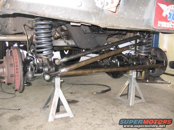 close-up of vehicle's front axle, suspension, and steering linkage, supported by jack stands