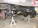 1988 Ford Bronco - The underside of a vehicle is shown, focusing on the front axle and suspension system, which is elevated on jack stands.
