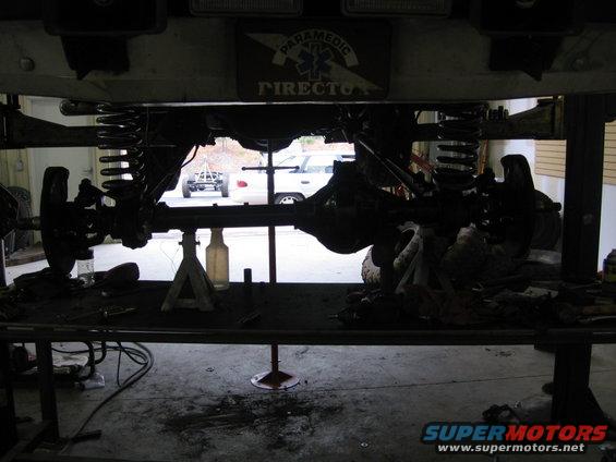 Undercarriage of a vehicle on jack stands, with another vehicle visible outside