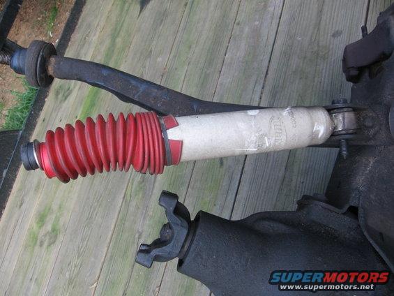 Shock absorber with red boot and U-joint on wooden surface