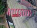 1988 Ford Bronco - Close-up of red coil spring and other suspension parts, likely for a vehicle, resting on a wooden deck.