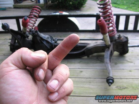 Front suspension parts with red springs and shocks, laid out on a wooden surface. A hand is in the foreground